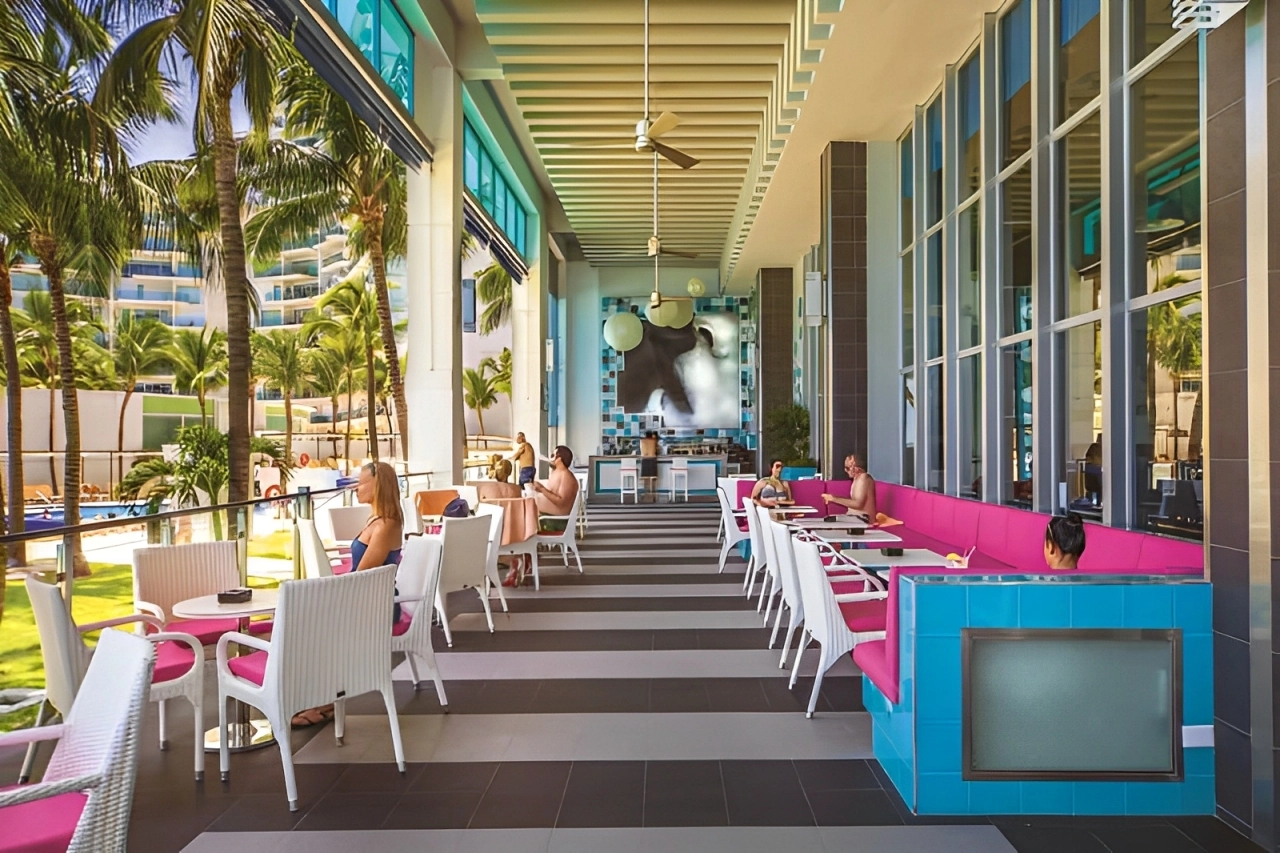 Outdoor dining terrace at Temptation Cancun Resort with bright pink and turquoise decor, surrounded by palm trees and pool views.