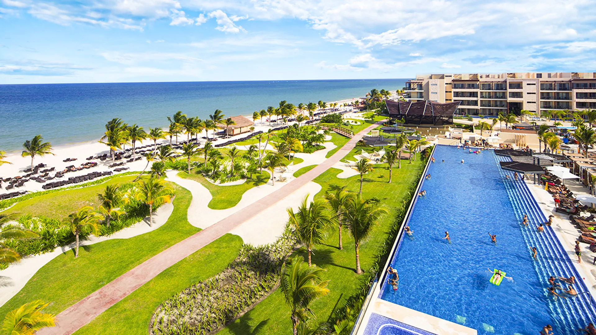 Aerial view of Temptation Cancun Resort showing a long infinity pool, lush gardens, and white-sand beachfront along the Caribbean Sea.
