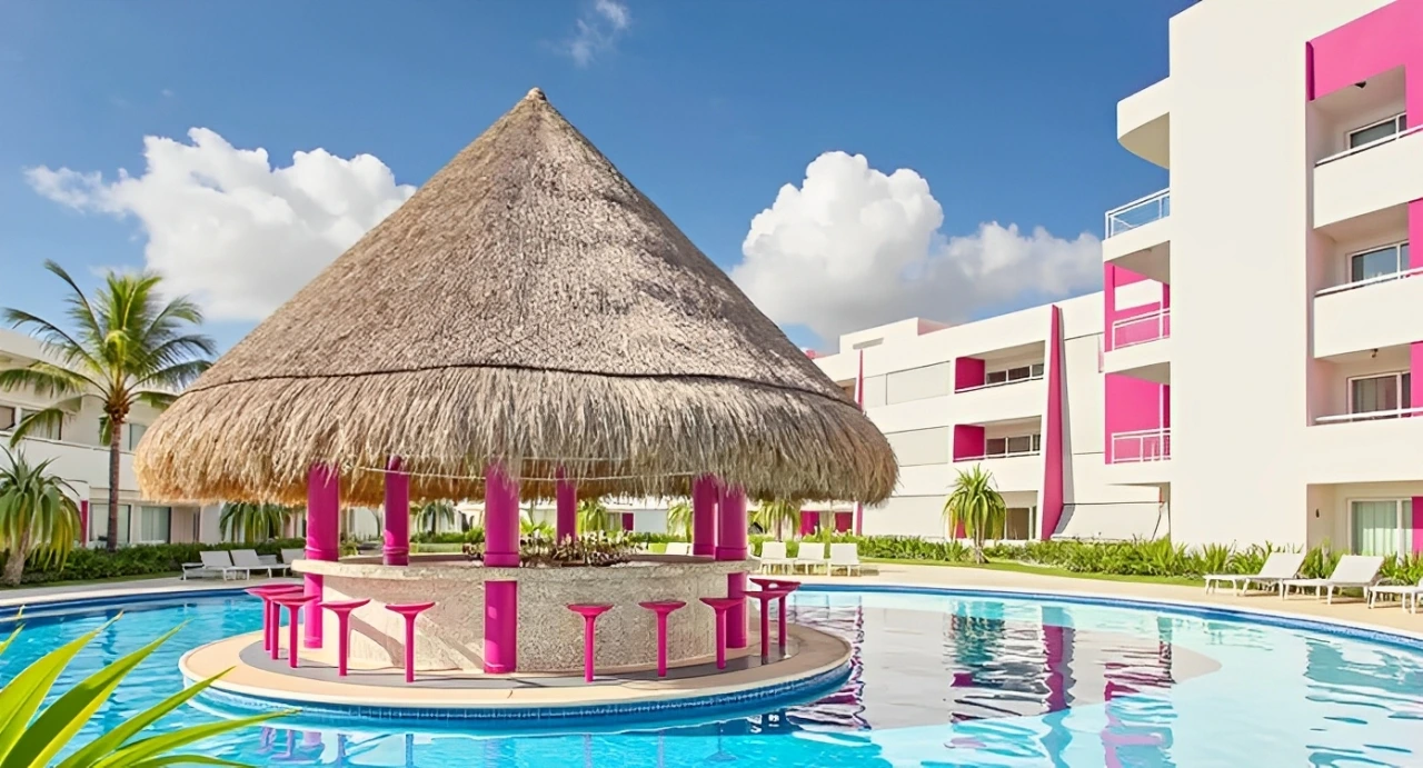 Thatched swim-up bar with pink accents at Temptation Cancun Resort surrounded by tropical palm trees and sunny blue skies.