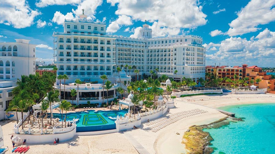 Aerial view of Riu Palace Cancun with beachfront pools, palm trees, and turquoise Caribbean water.