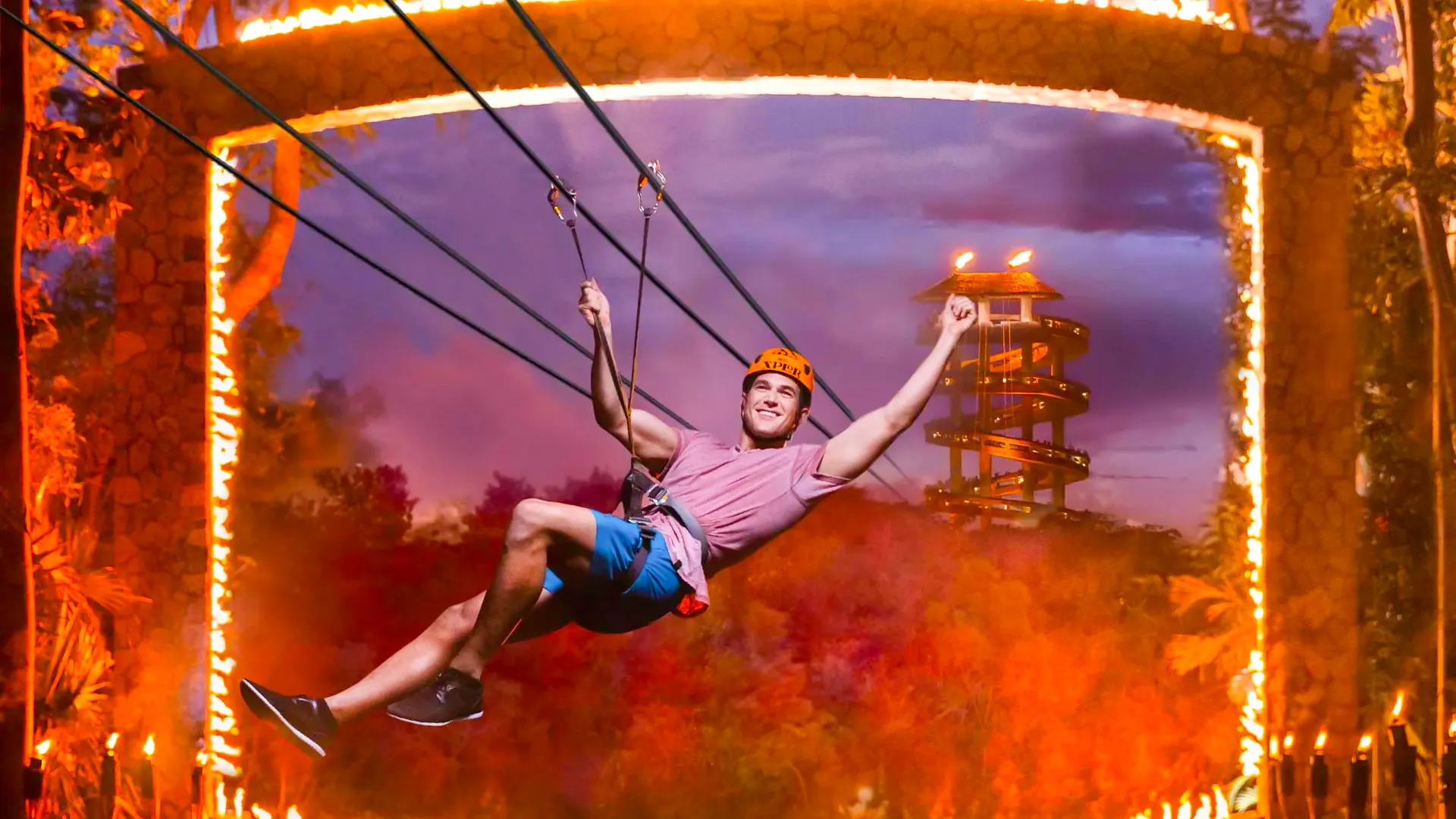 Man ziplining through a fiery ring at sunset during the Xplor Fuego night adventure.