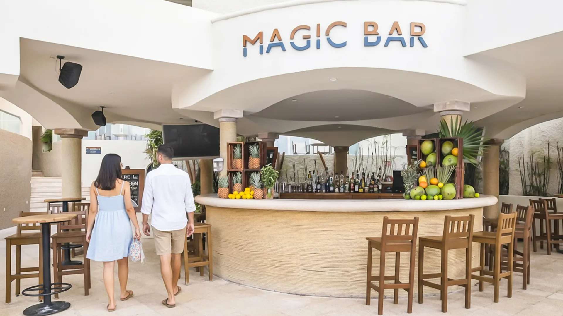  A couple walking towards the Magic Bar at a resort, surrounded by tropical fruit decorations at the bar.