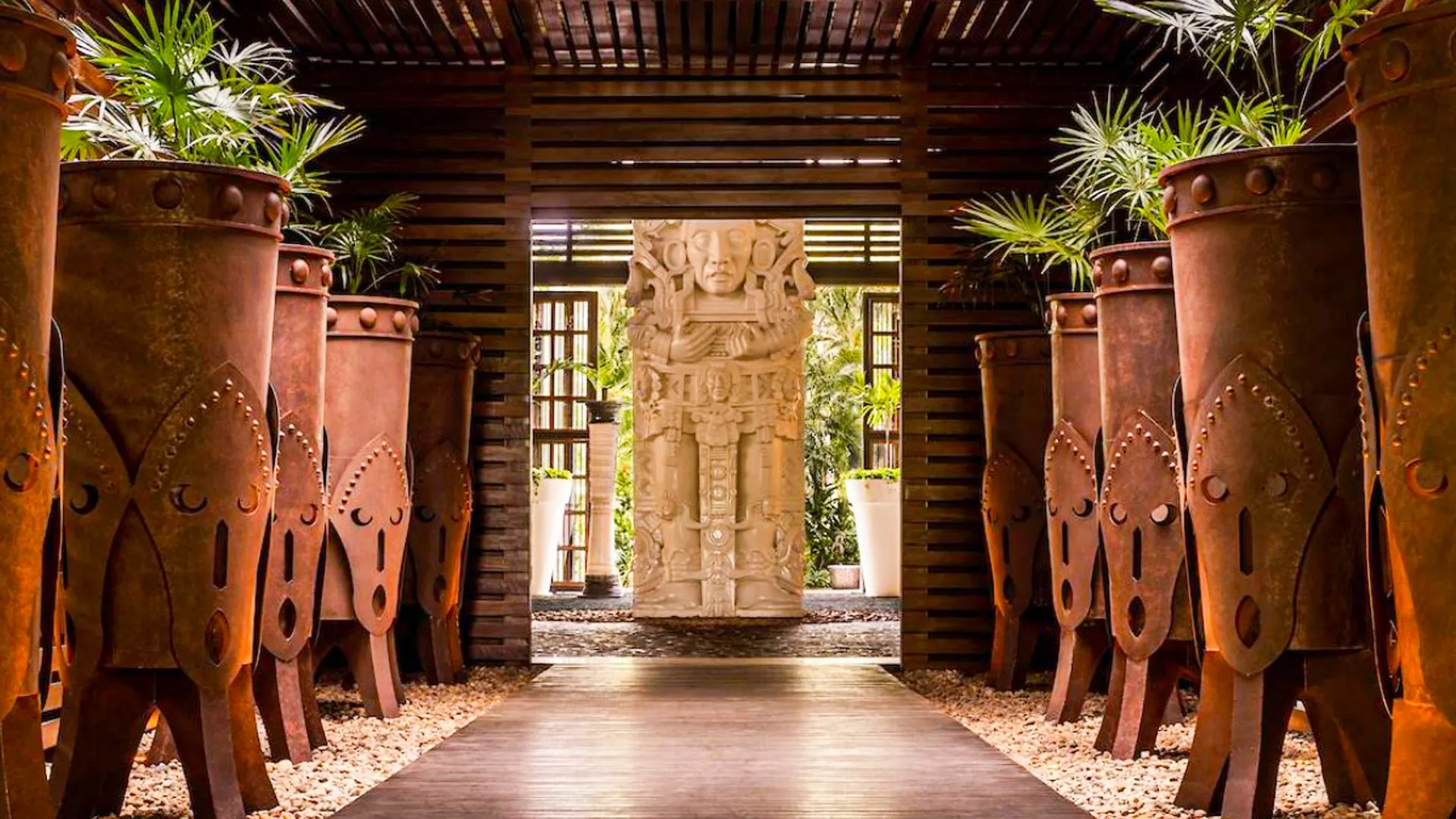 Hallway at Vidanta Riviera Maya decorated with large terracotta vases and a Mayan stone statue at the end. 