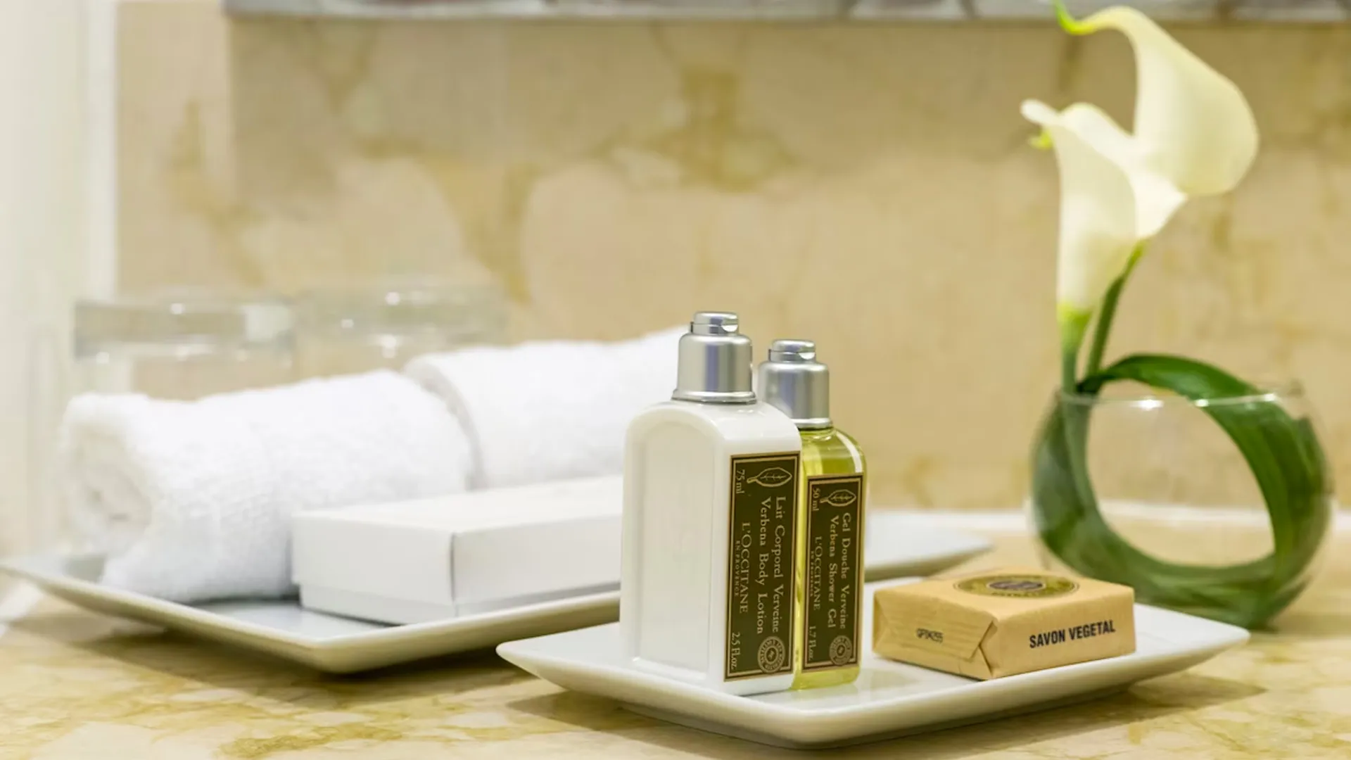 Close-up of luxurious toiletries at Sun Palace Cancun, including bottles of lotion, soap, and fresh white towels, with a decorative flower in the background.