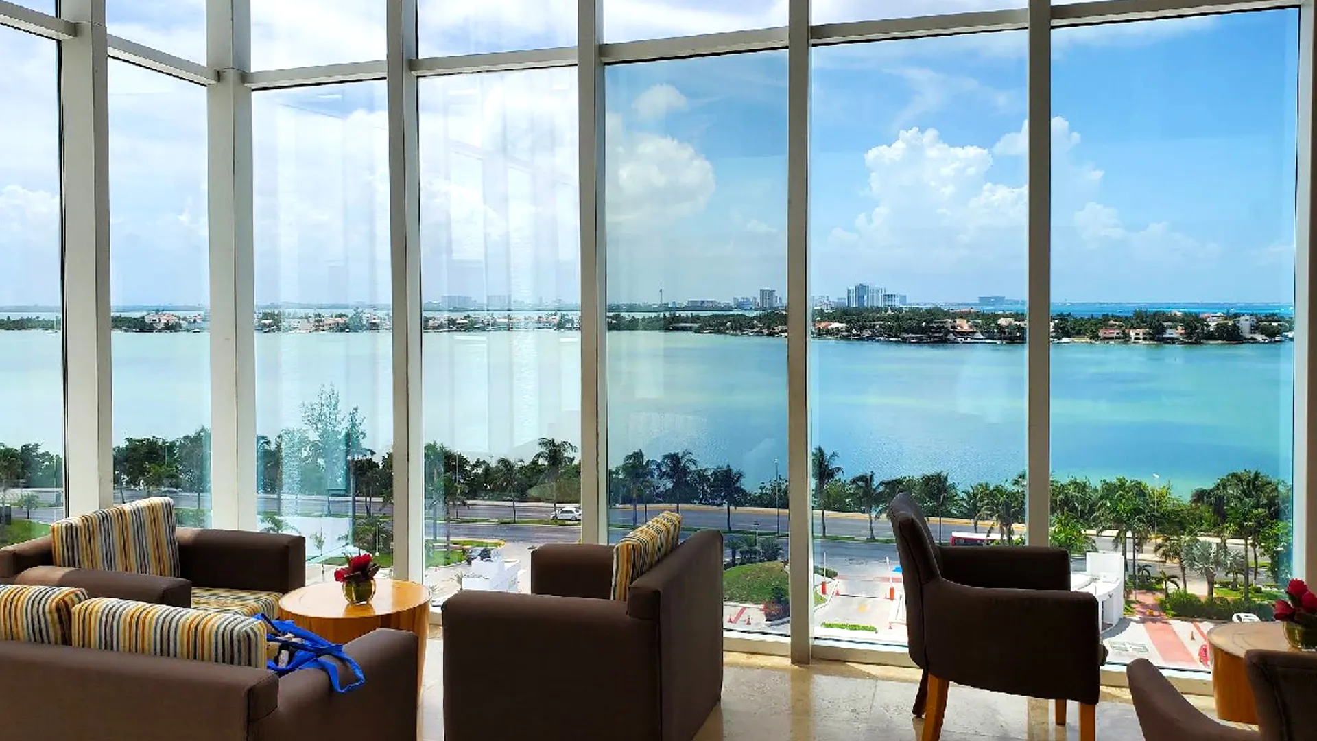 A modern room with large windows offering a panoramic view of a lagoon and distant skyline under a bright blue sky.
