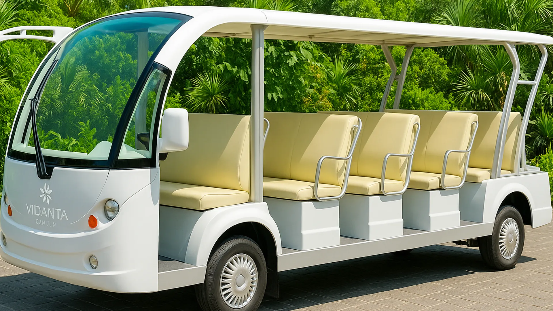 A white open-air shuttle bus with "Vidanta Cancun" branding, featuring beige cushioned seats and a sleek design, parked on a paved area with lush green foliage in the background.