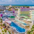 An aerial view of Temptation Cancun Resort with colorful buildings, a large pool, beachfront, palm trees, and the turquoise ocean.