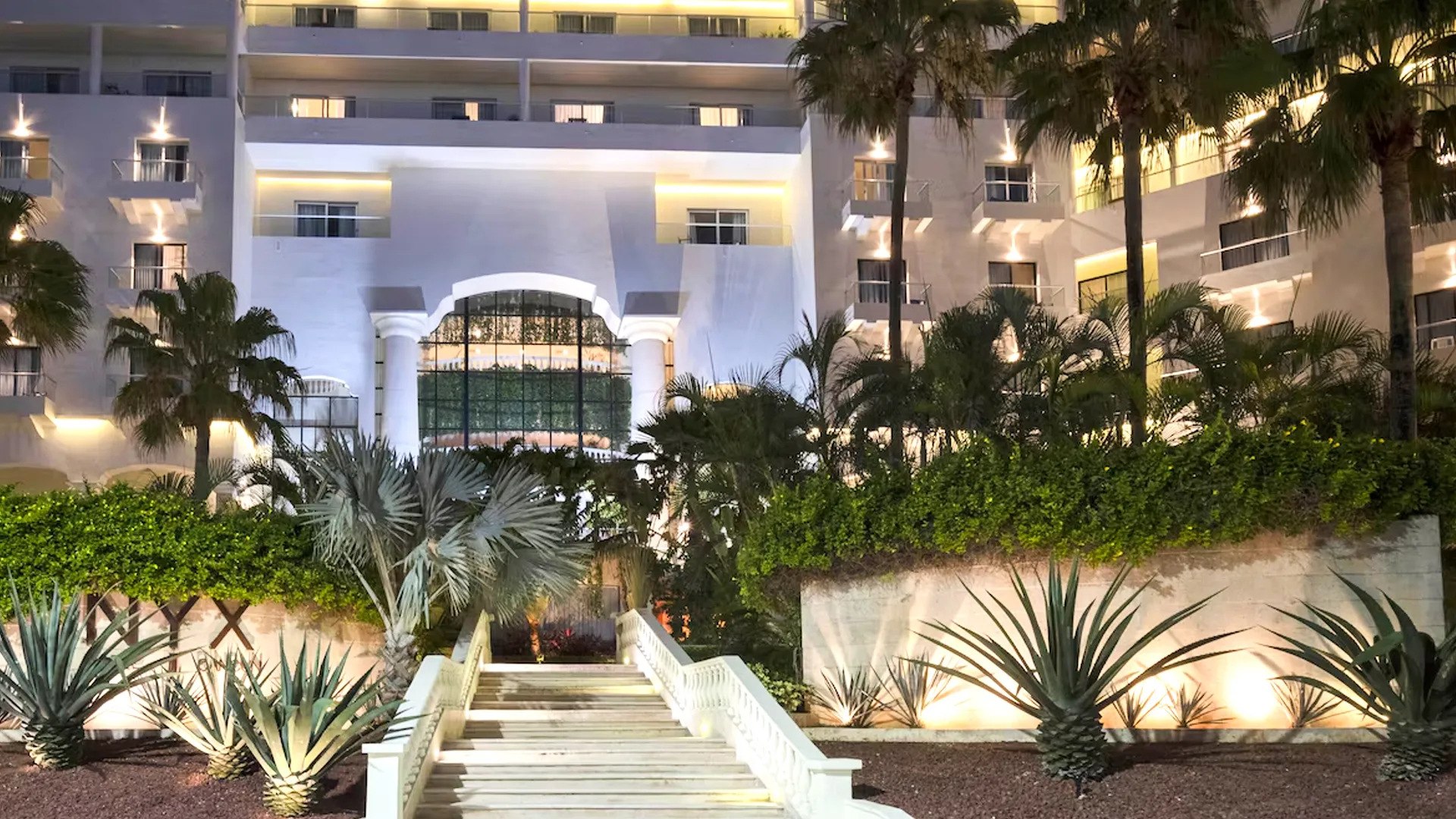  Night view of Hotel NYX Cancun entrance illuminated with tropical palm trees and modern architecture. 
