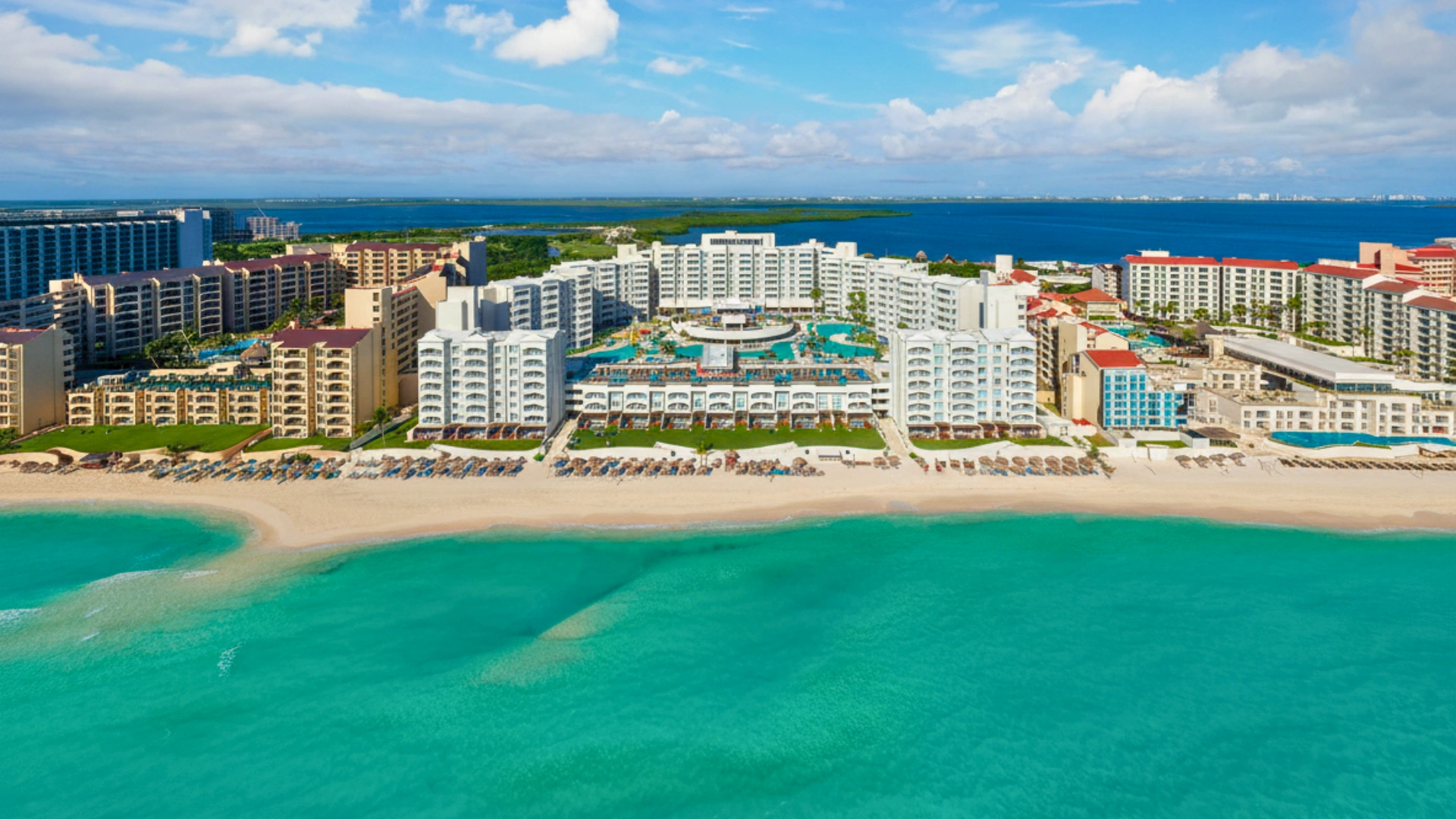 An aerial view of a luxury resort with multiple pools, palm trees, and a pristine beach with crystal-clear water.