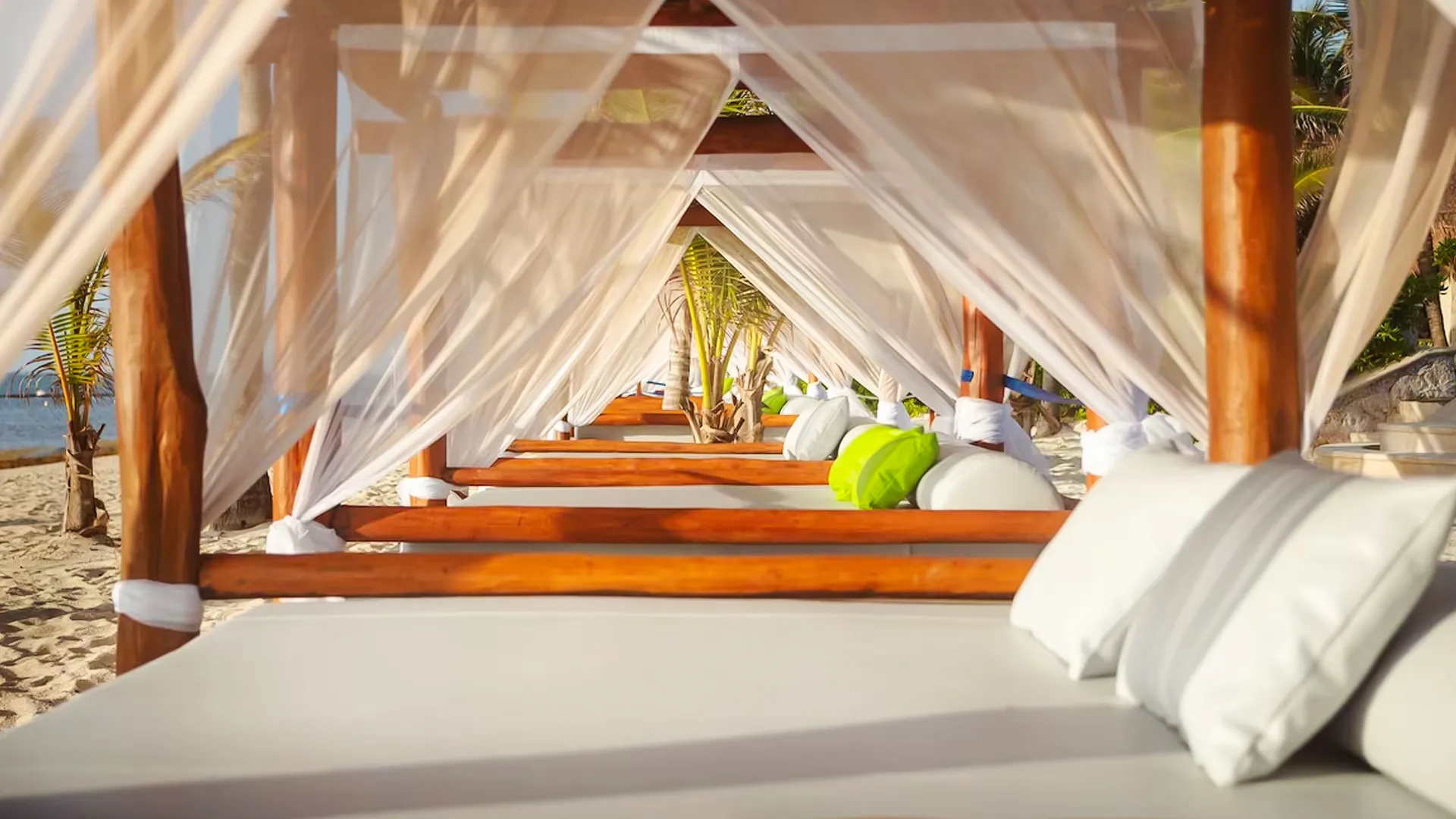 Beach cabanas with white curtains and lounge beds at Margaritaville Island Reserve Riviera Cancun facing the ocean.