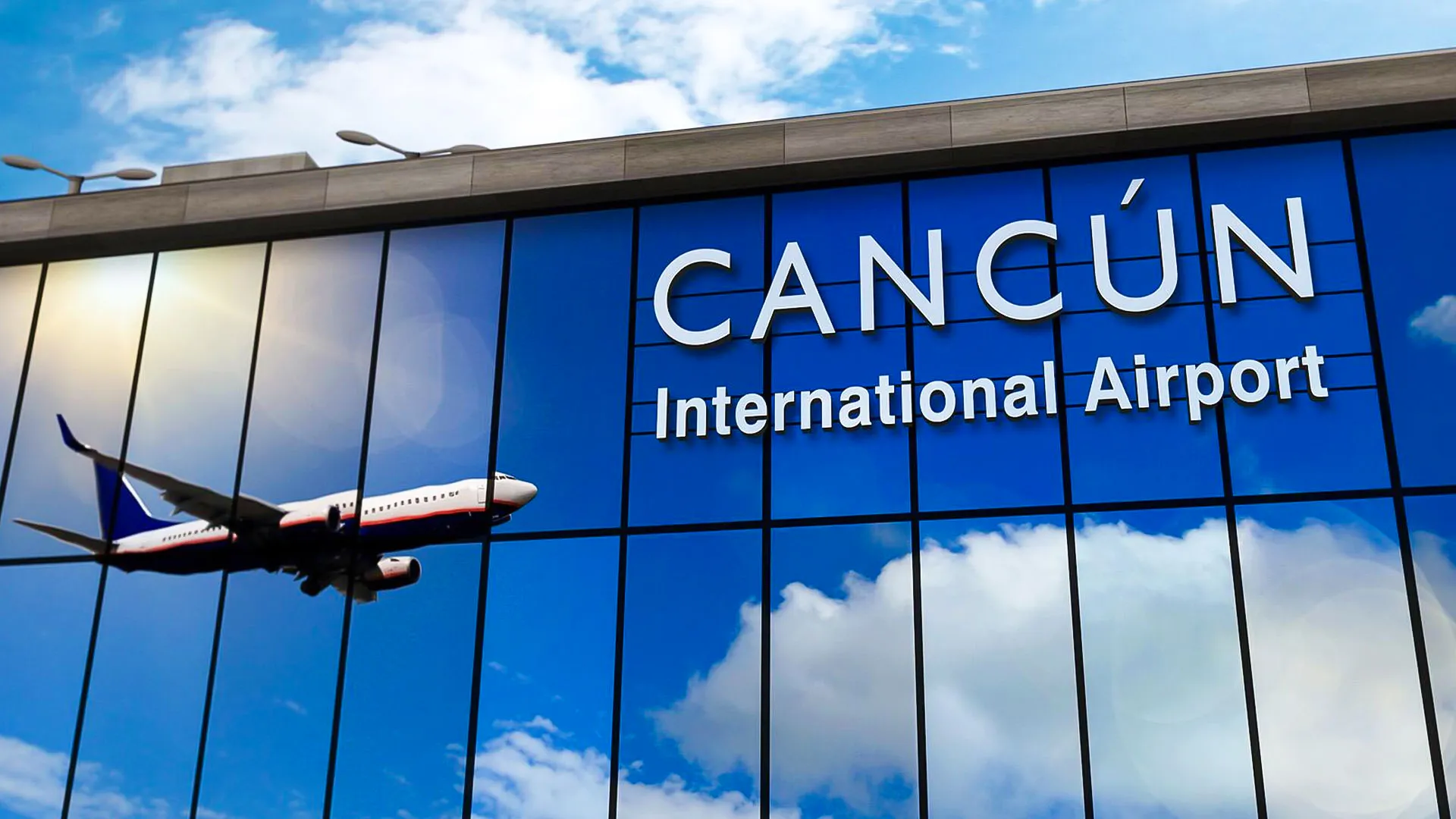 Exterior view of Cancun International Airport with a plane flying overhead and blue glass facade reflecting the sky.