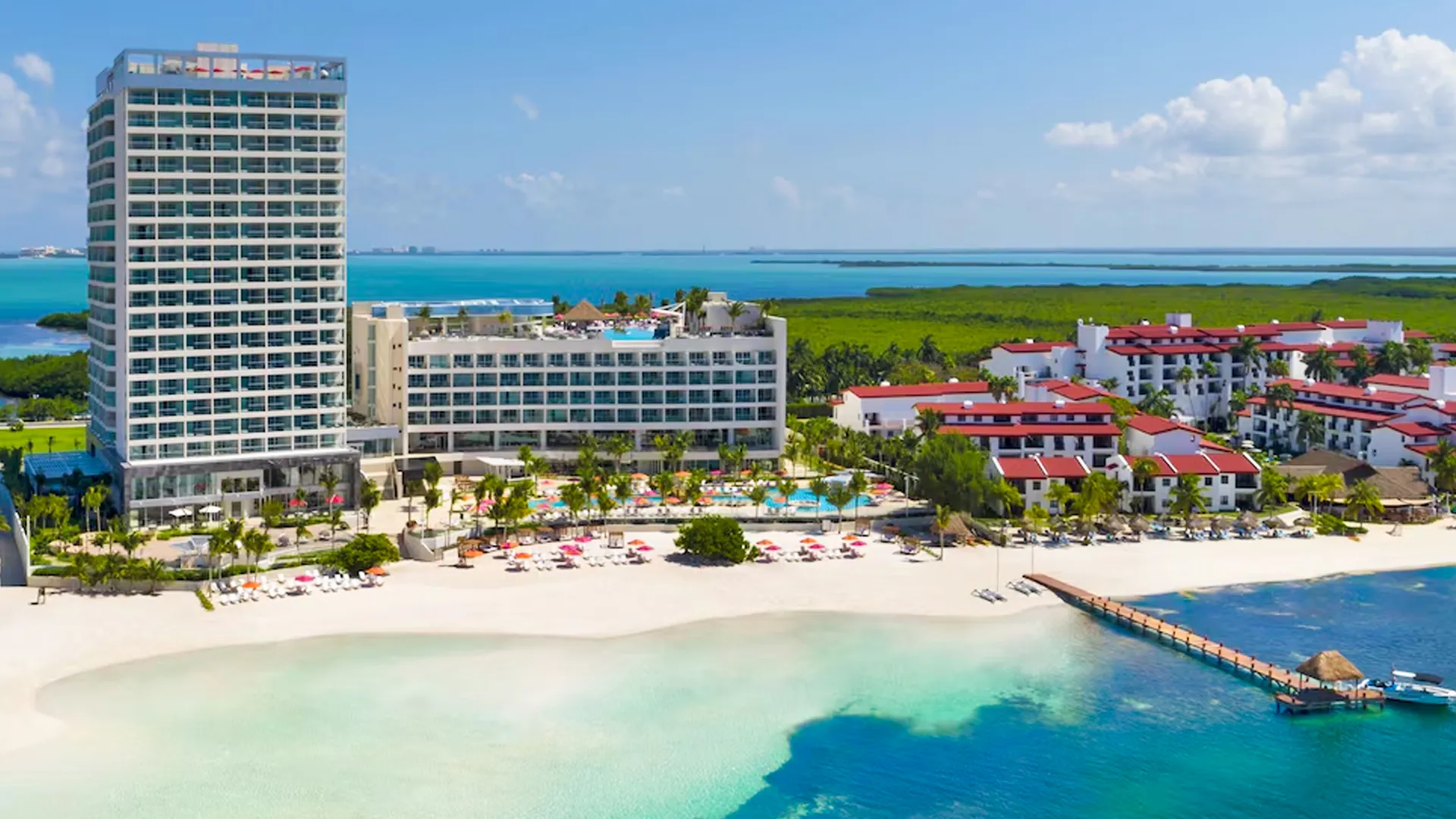 Aerial view of Breathless Cancun Soul resort featuring a tall oceanfront tower, white sand beach, turquoise water, and nearby red-roofed villas.