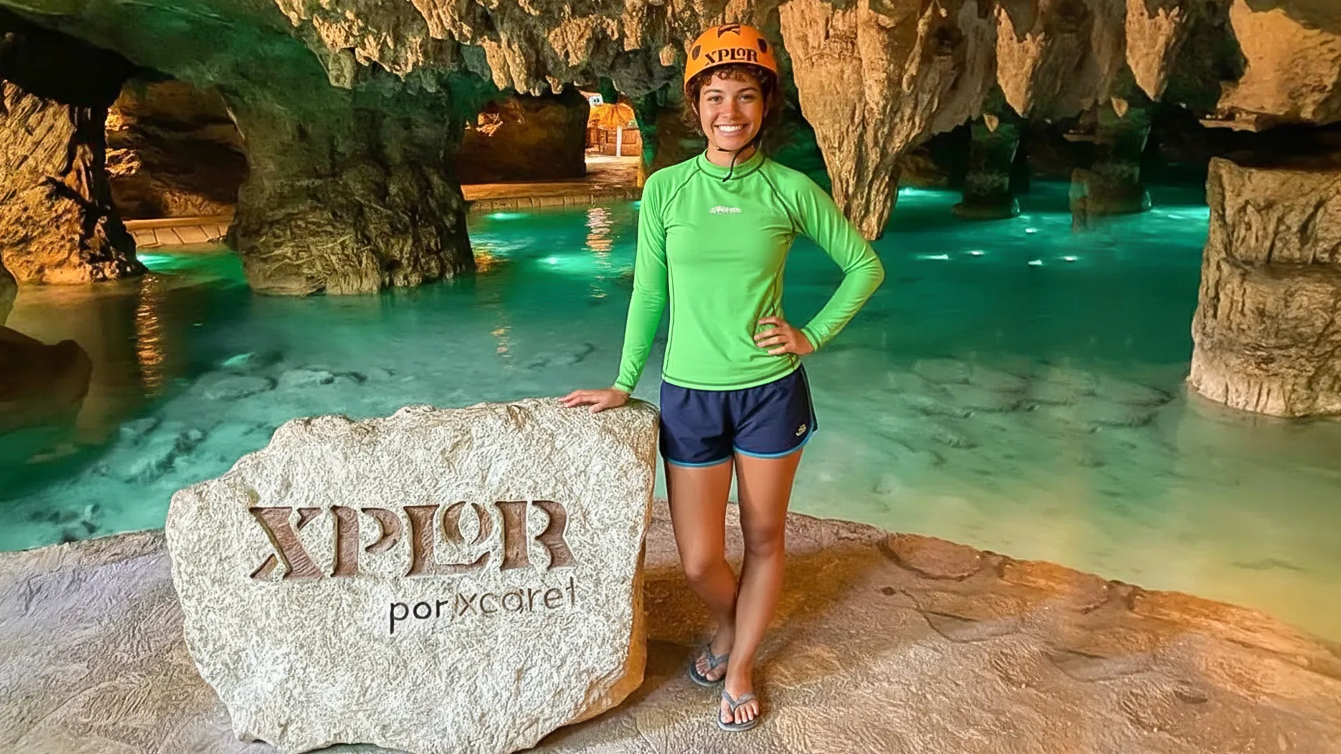 Woman in life vest entering a glowing underground river surrounded by stalactites at Xplor Park.