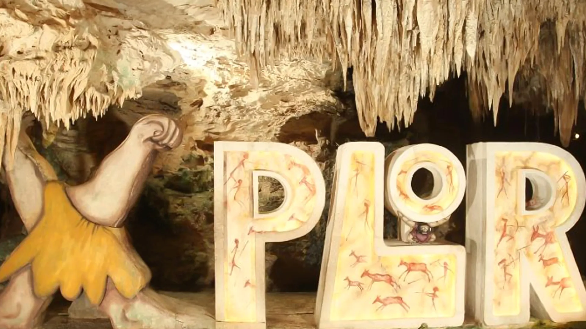 Large “Xplor” sign carved inside a limestone cave surrounded by stalactites.