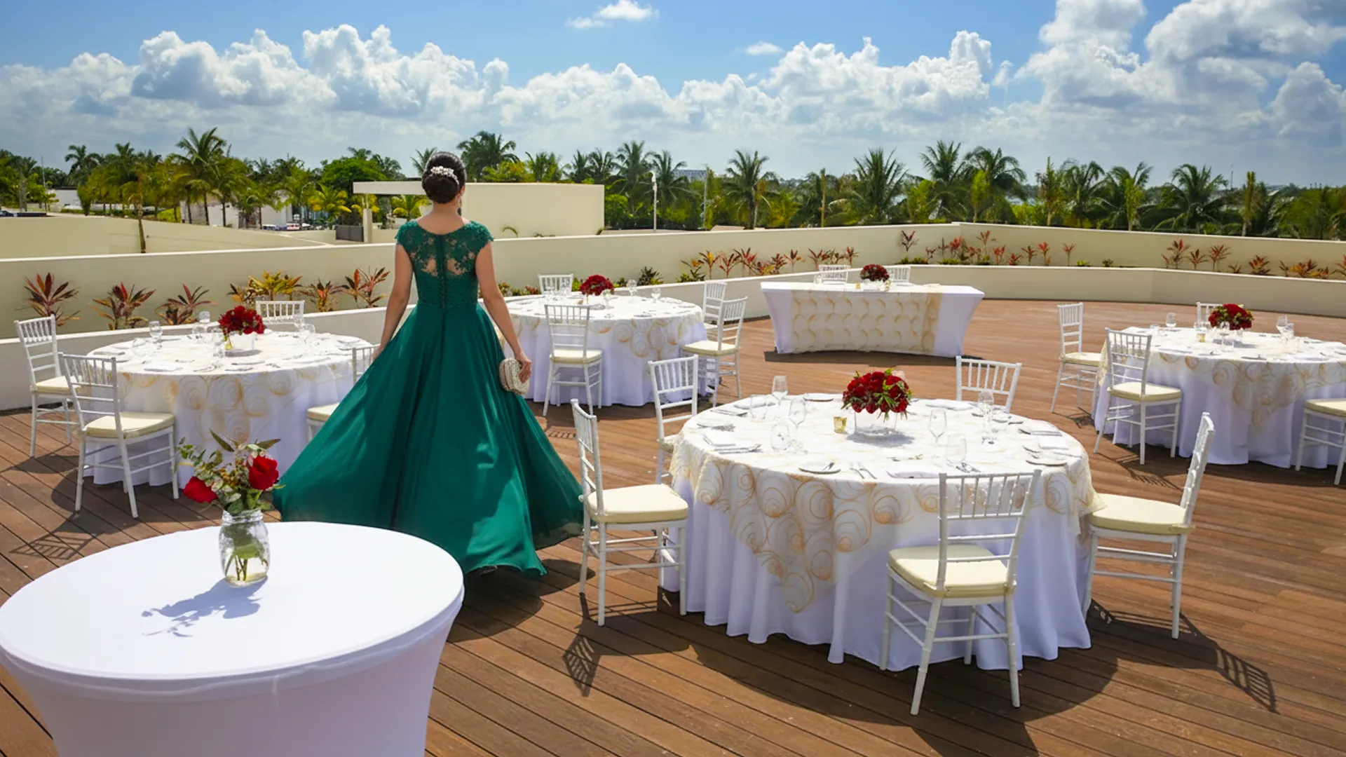 Elegant woman in green gown walking toward rooftop event tables at Royalton Riviera Cancun.