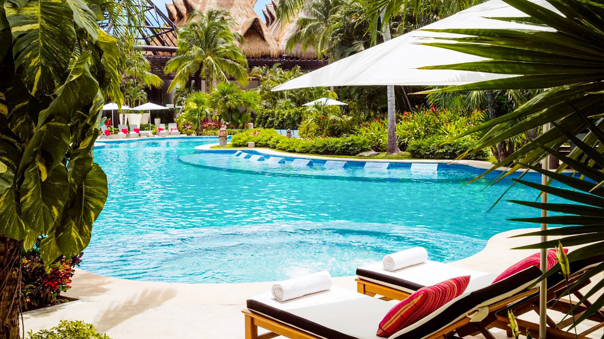 Poolside view at Vidanta Riviera Maya with tropical plants, lounge chairs, and turquoise water under white umbrellas. 