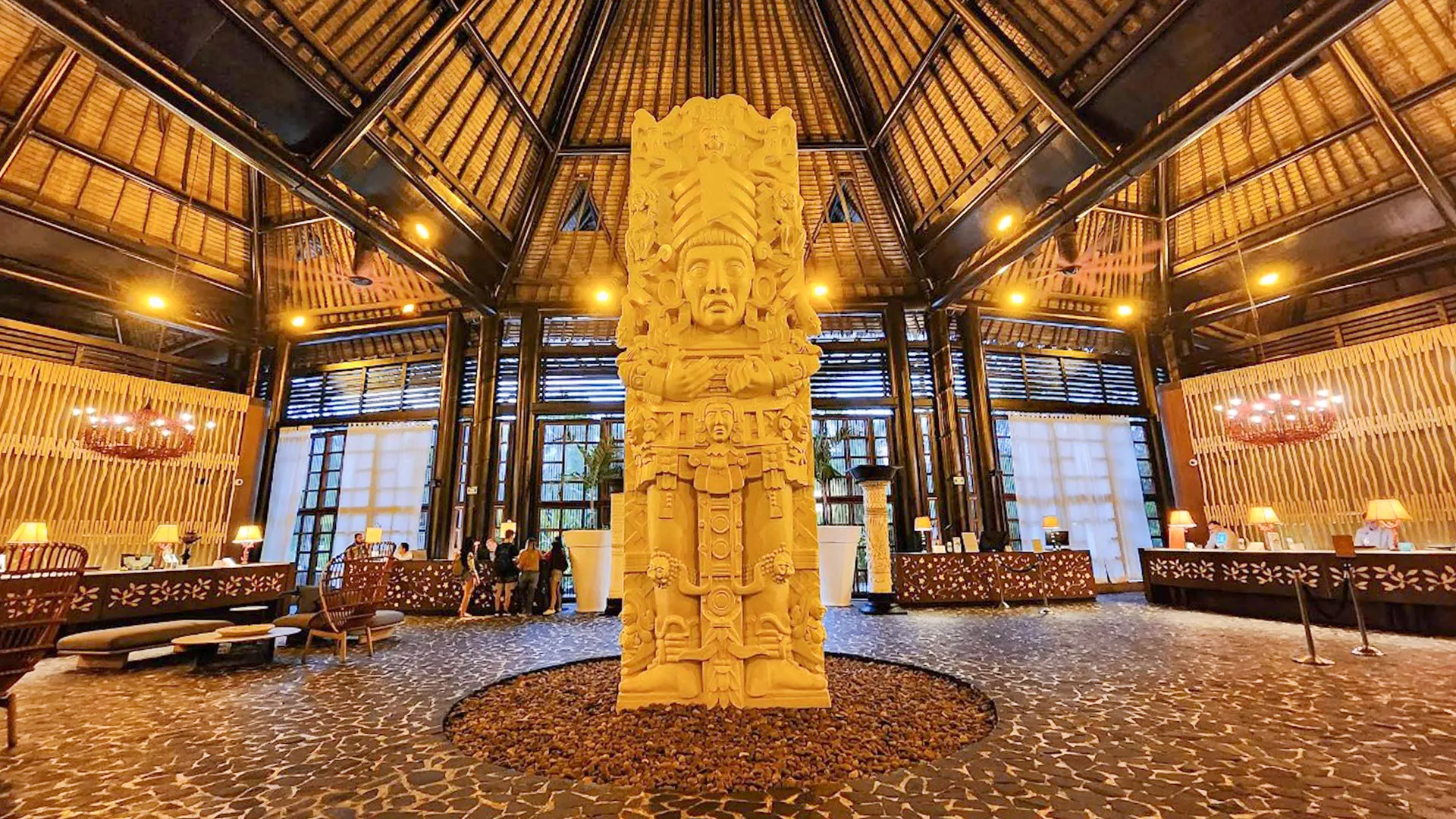Lobby of Vidanta Riviera Maya featuring a grand Mayan-style stone sculpture under a high thatched roof.