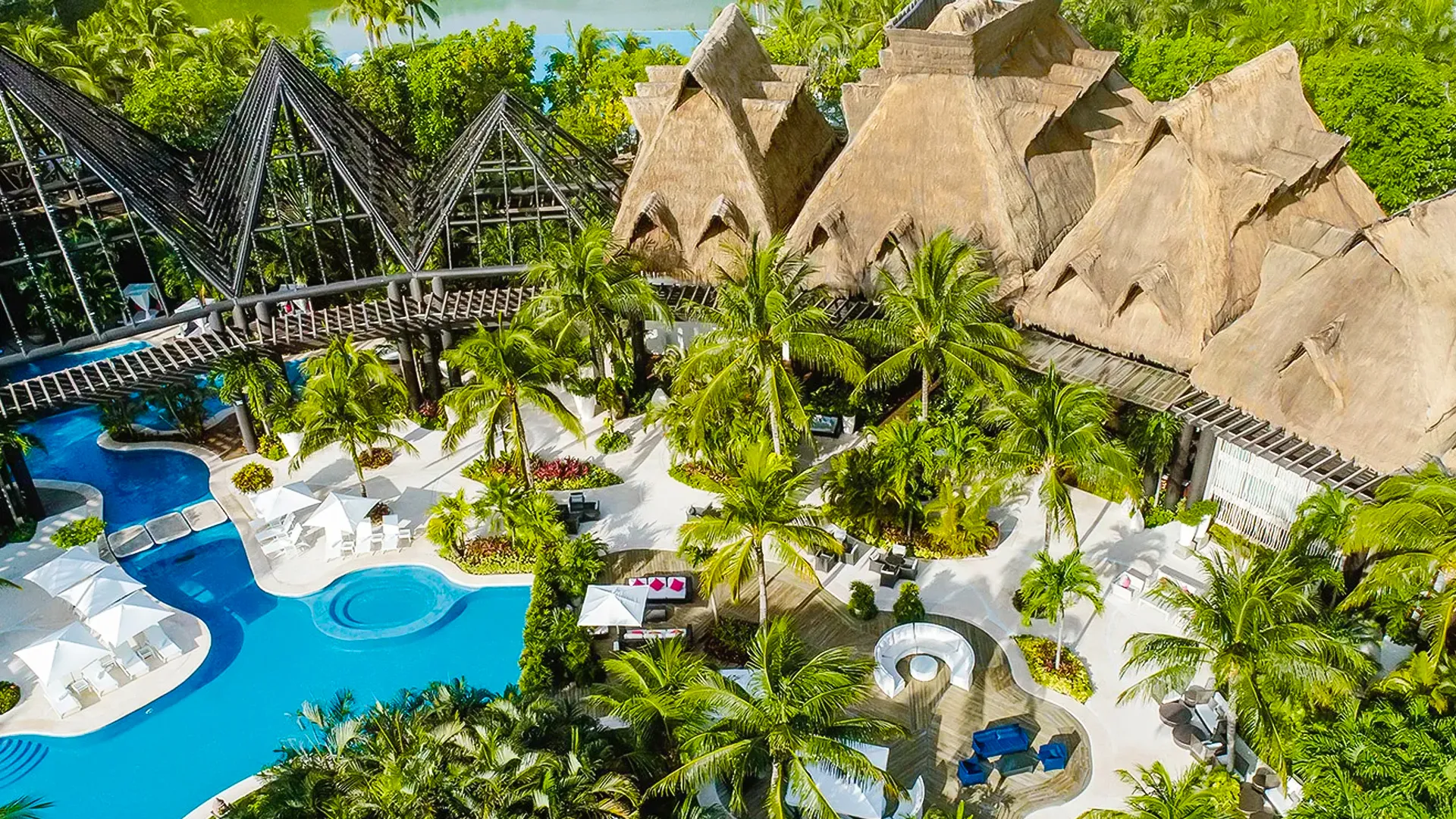 Aerial view of Vidanta Riviera Maya with pyramid-style buildings, lush palm gardens, and winding blue pools.