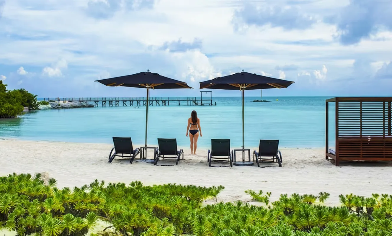Woman walking toward the turquoise sea at Nizuc Resort Cancun’s private beach with sun loungers and umbrellas.