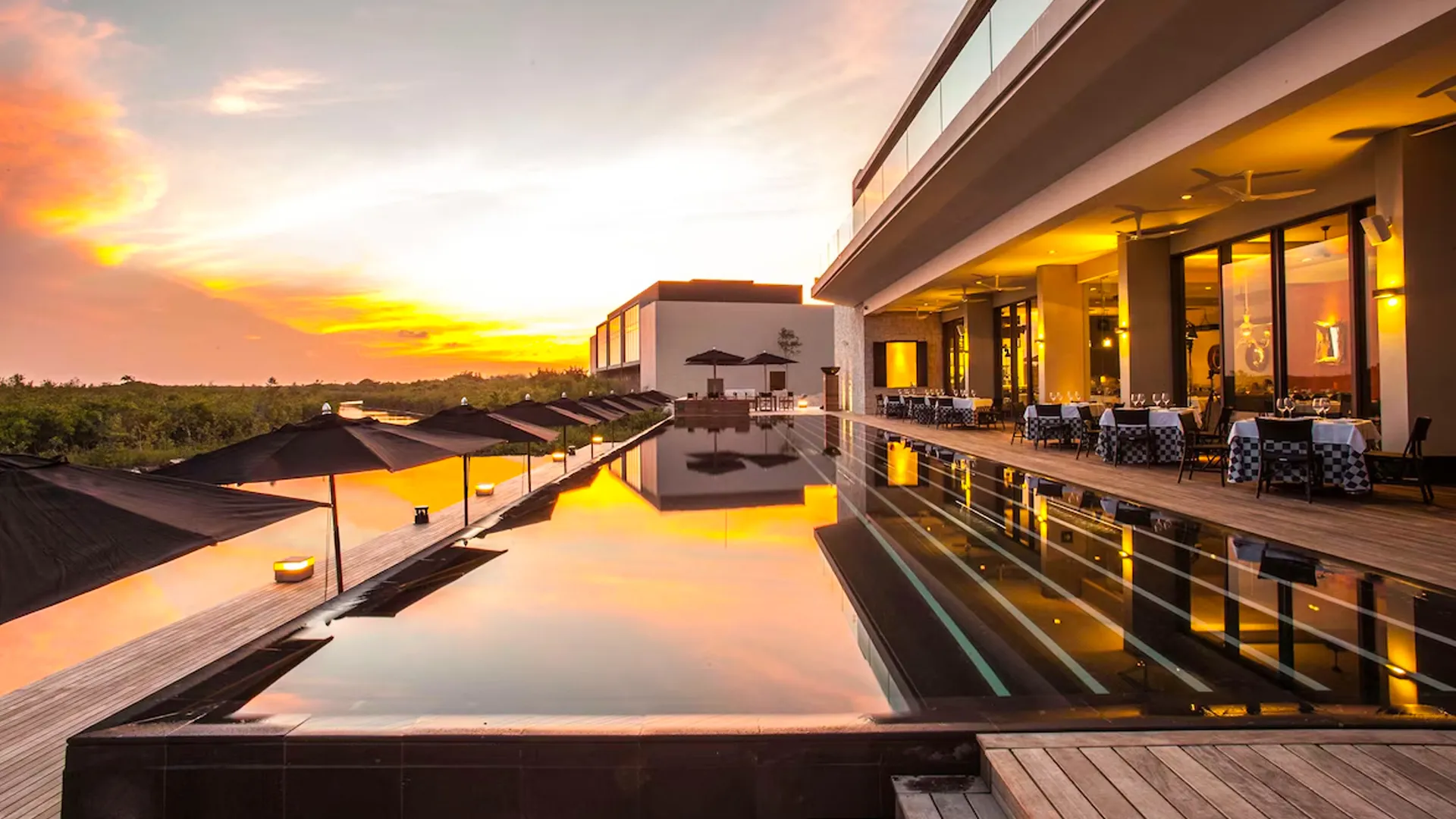 Infinity pool at Nizuc Resort Cancun reflecting a golden sunset, surrounded by cabanas and dining areas.