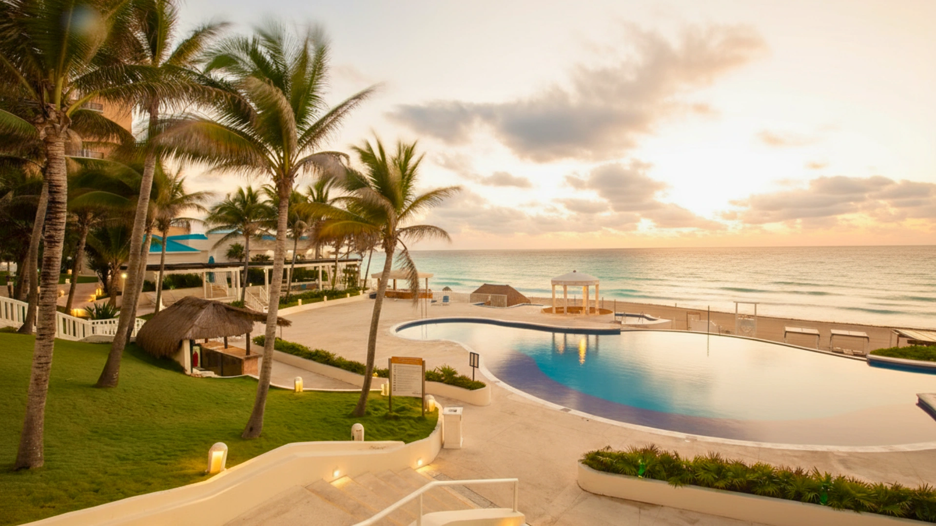 Pool area at Golden Parnassus Cancun with palm trees, sunset sky, and ocean view.