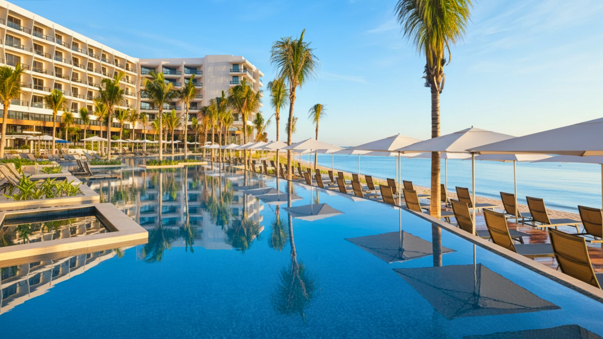 Luxury beachfront pool at Hilton Cancun All-Inclusive Resort surrounded by palm trees, sun loungers, and ocean views under a clear blue sky.