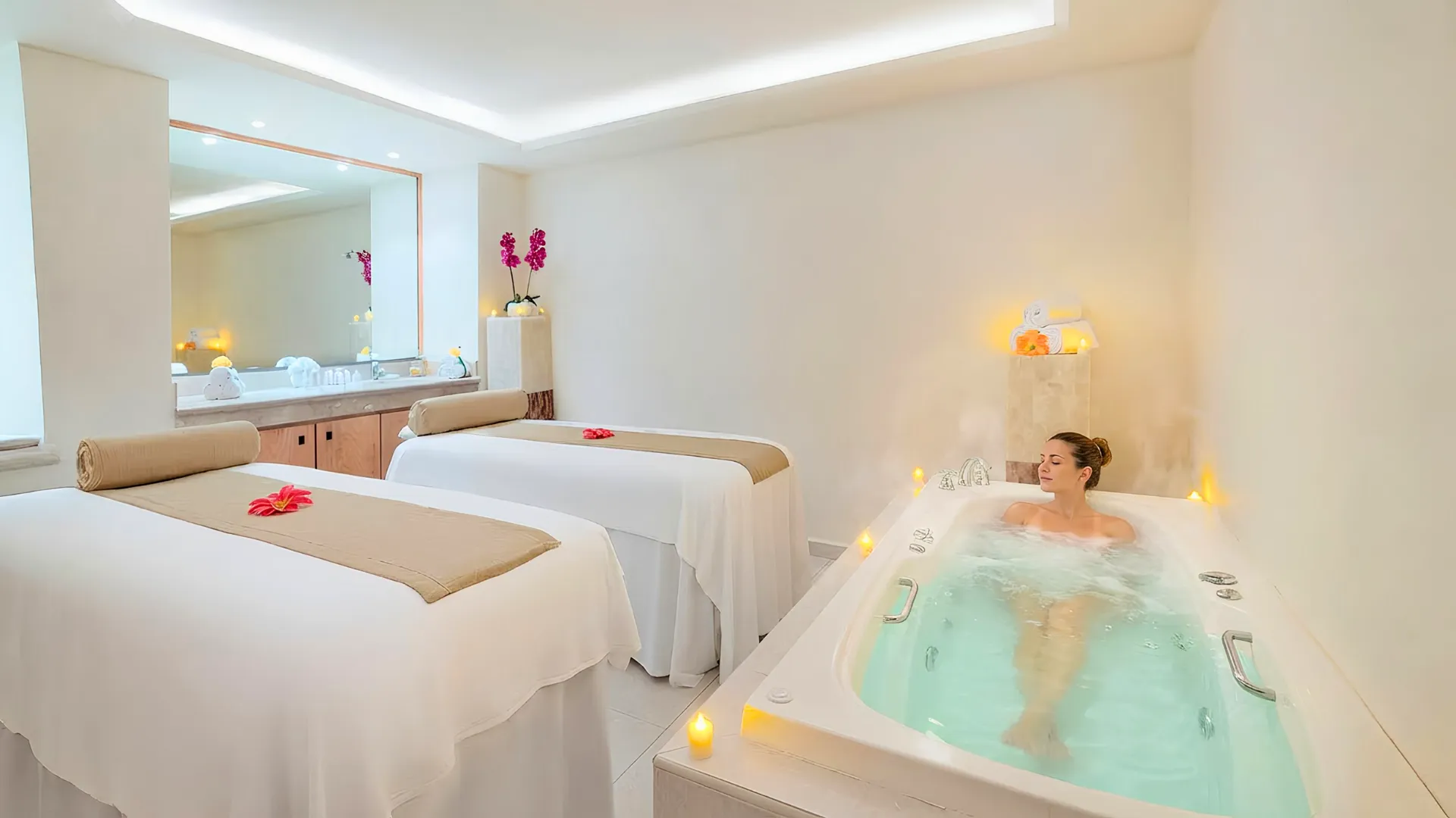 Spa room at Royal Solaris Cancun with two massage beds, soft lighting, flowers, and a woman relaxing in a jacuzzi.