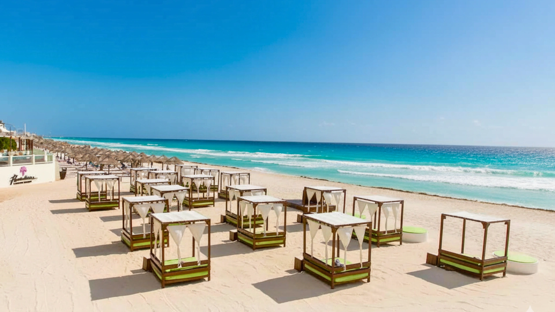  A pristine beach with thatched cabanas and lounge chairs along the shoreline under a clear blue sky.