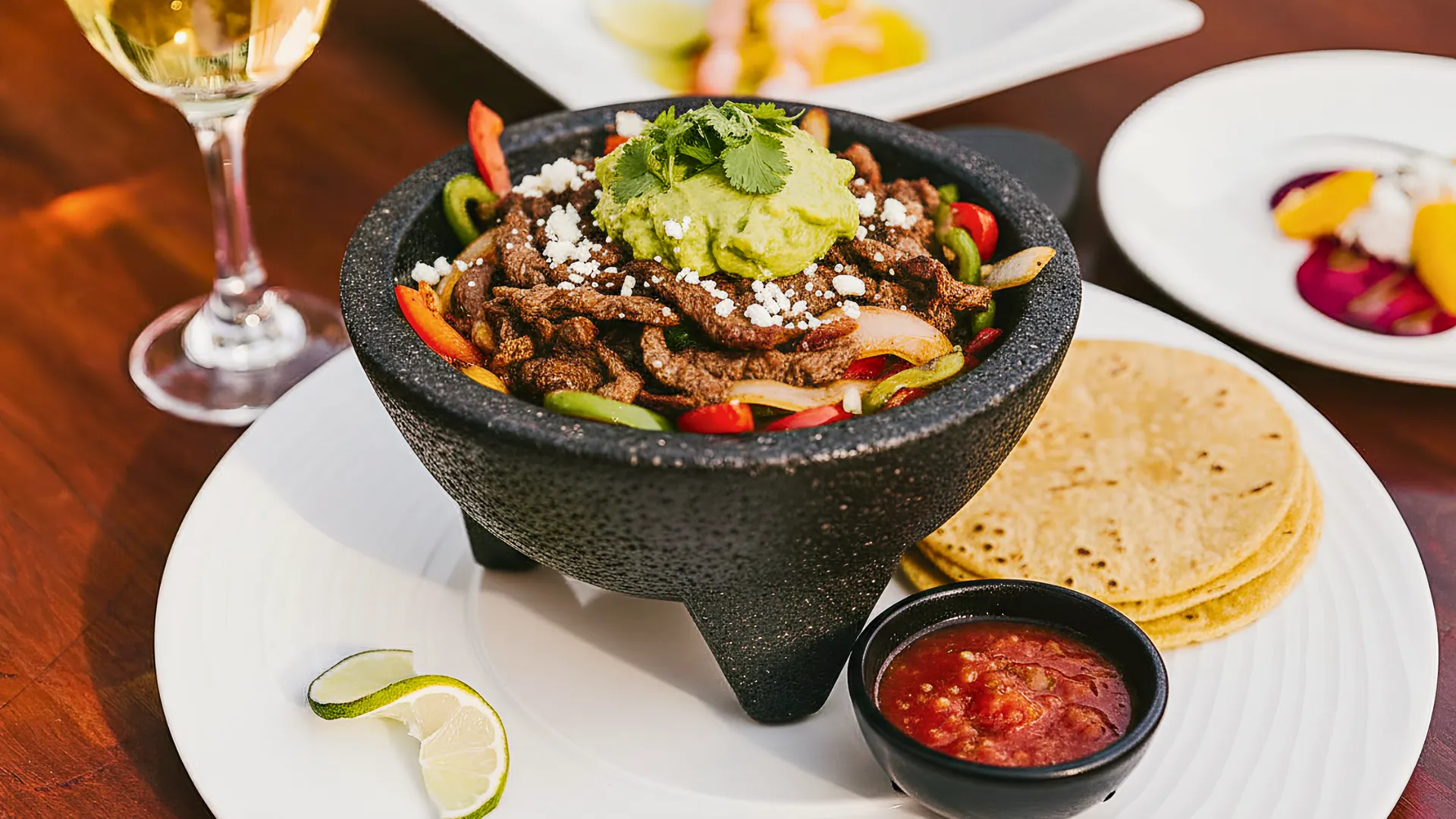 A delicious, colorful plate of sizzling fajitas served in a molcajete, featuring grilled meat, bell peppers, onions, and fresh guacamole.