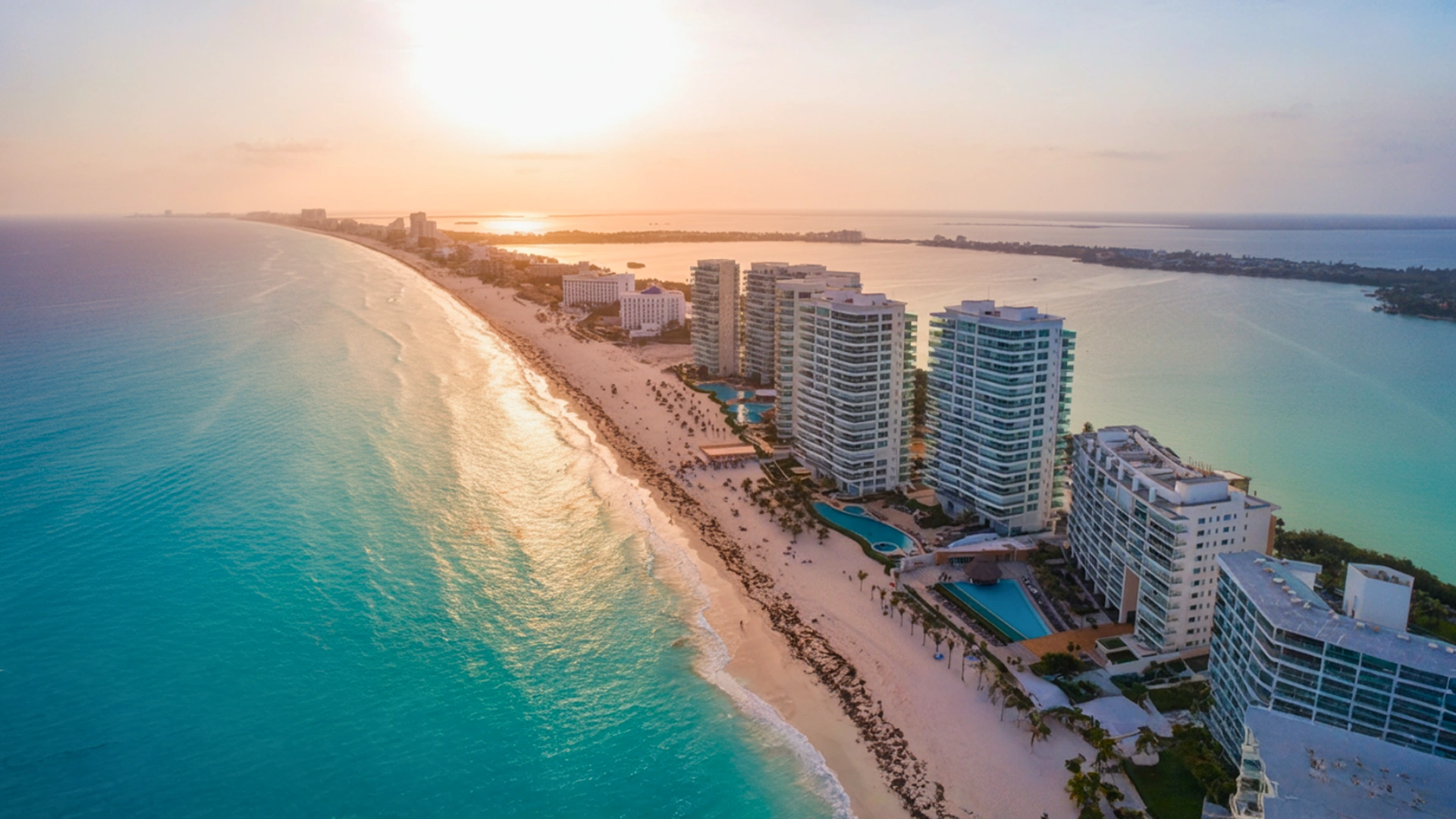  Aerial view of Sandos Cancun resort at sunset with high-rise buildings, beach, and pools.
