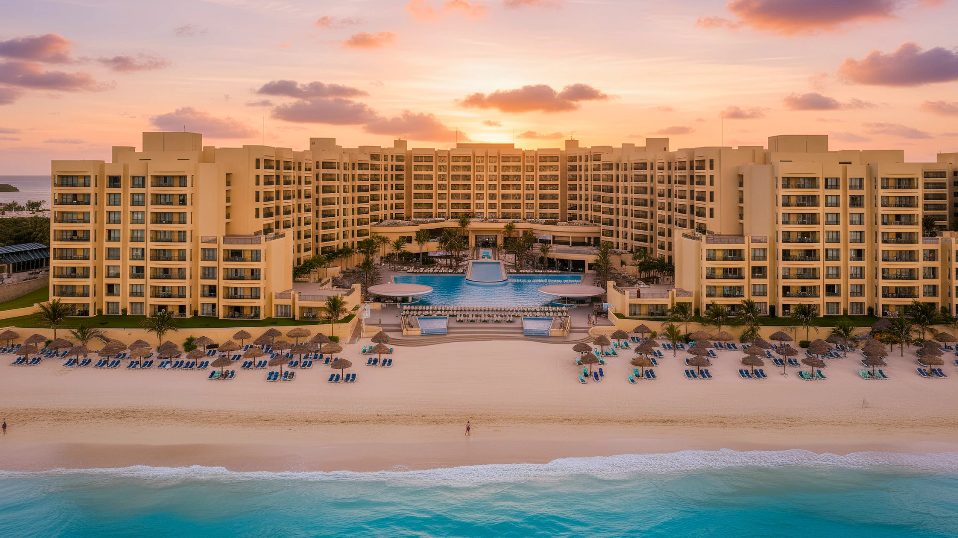 The Royal Sands Cancun resort viewed from the beach at sunset, with loungers lined up on the sand.
