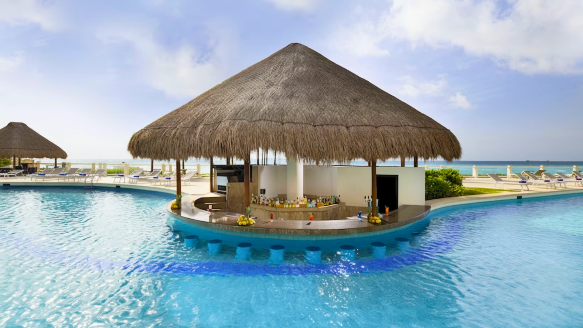  A tropical bar with a thatched roof situated in the middle of a swimming pool, surrounded by lounge chairs and palm trees under a partly cloudy sky.
