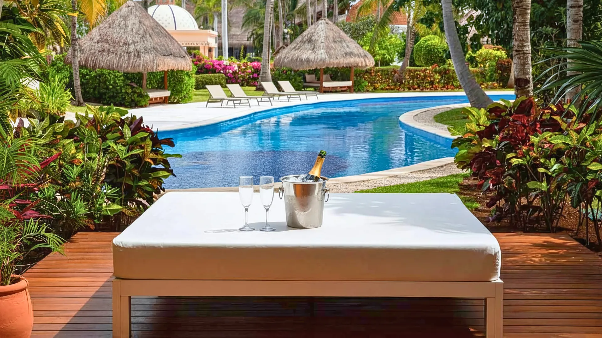  A table set with champagne glasses by the poolside, surrounded by vibrant tropical plants and a serene view of the pool.