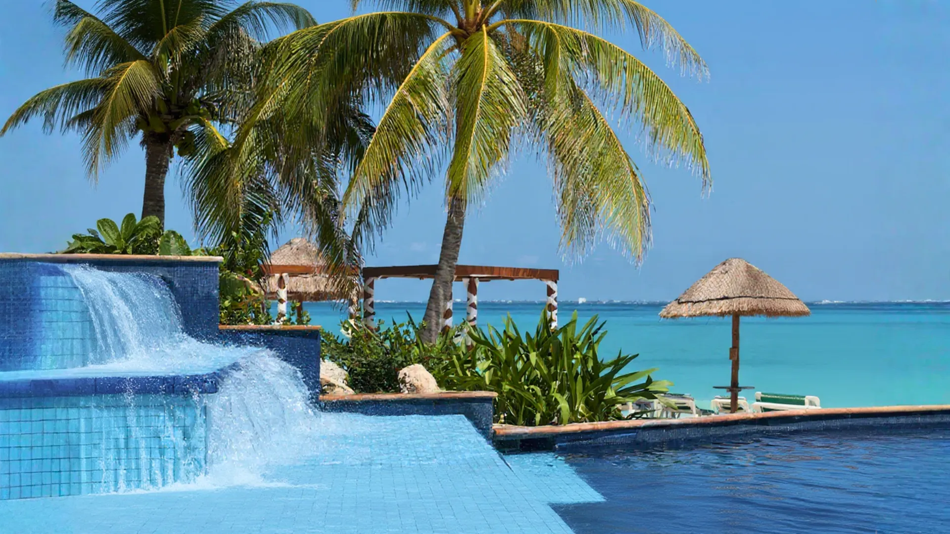 Infinity-style pool with cascading waterfall and palm trees at Grand Fiesta Americana Coral Beach Cancun overlooking the Caribbean Sea.