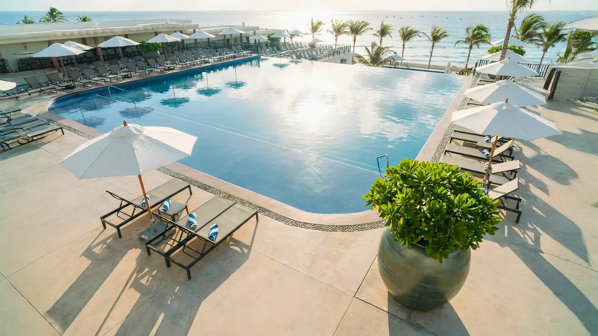 Large infinity-style main pool at Seadust Cancun overlooking the ocean, surrounded by loungers, umbrellas, and palm trees.