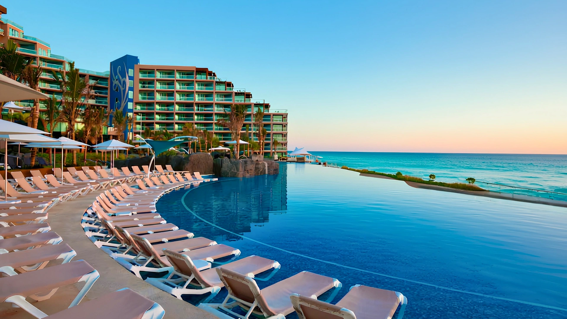 Infinity pool with loungers at Hard Rock Cancun resort overlooking turquoise ocean at sunset.