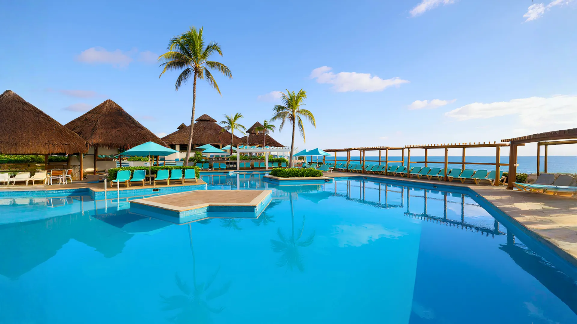 Outdoor pool area at Royal Solaris Cancun with thatched-roof cabanas, palm trees, turquoise loungers, and a bright blue sky.