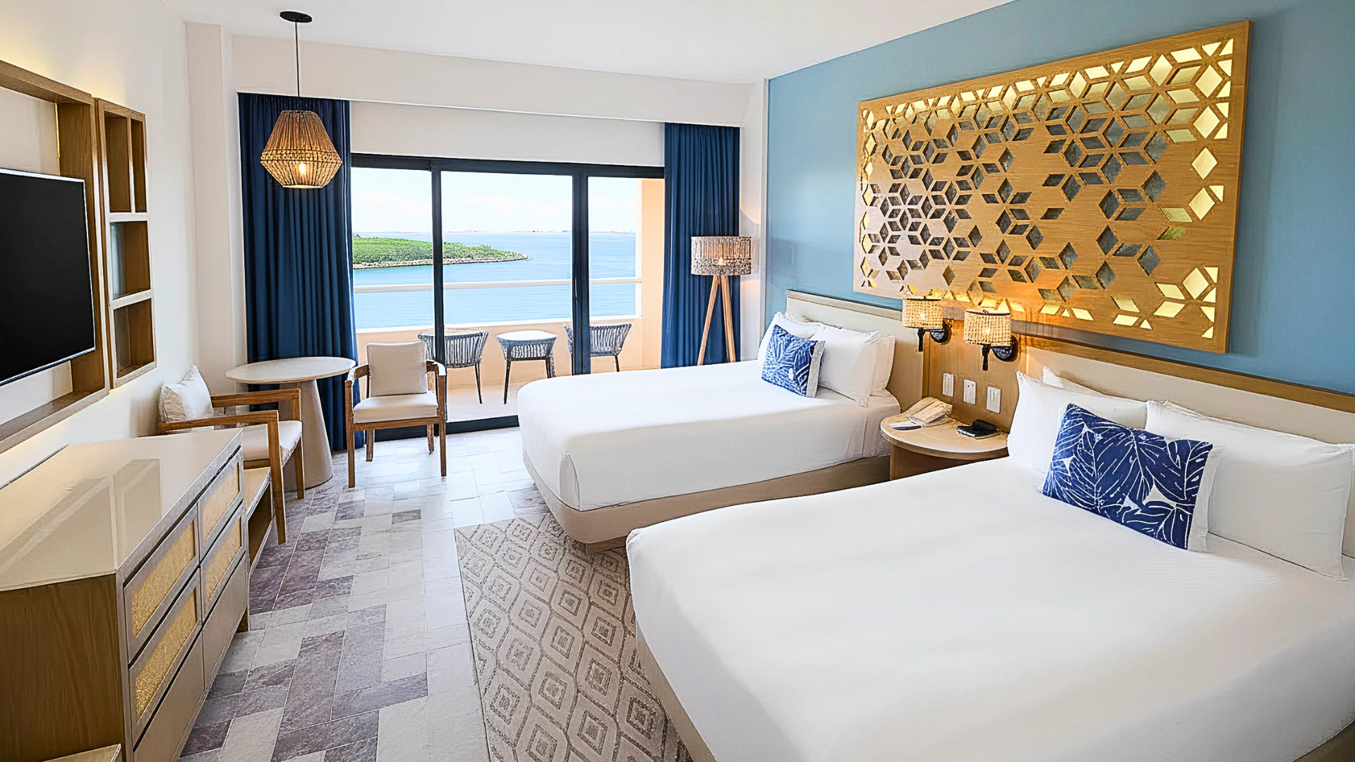 A modern hotel room with two double beds, ocean-view balcony, blue accents, and elegant wooden décor.
