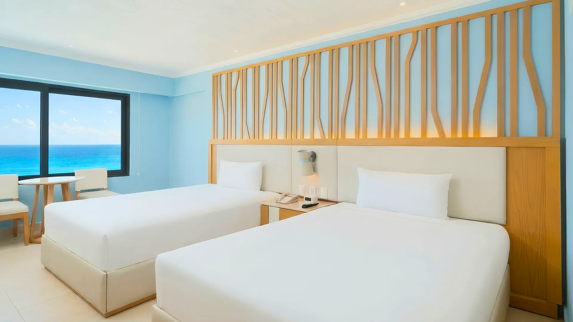 Modern double room at Royal Solaris Cancun with two white beds, light-blue walls, wood accent headboard, and oceanview window.