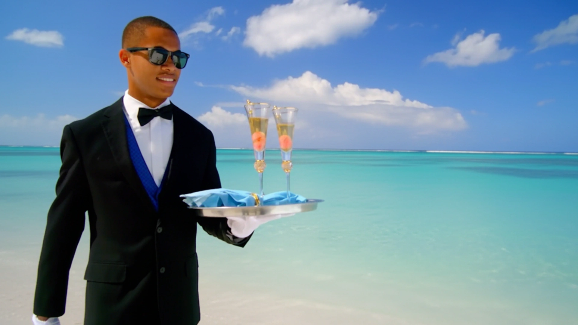 Hotel staff member in formal uniform serving champagne on the beach at Hilton Cancun All-Inclusive Resort with turquoise sea background.