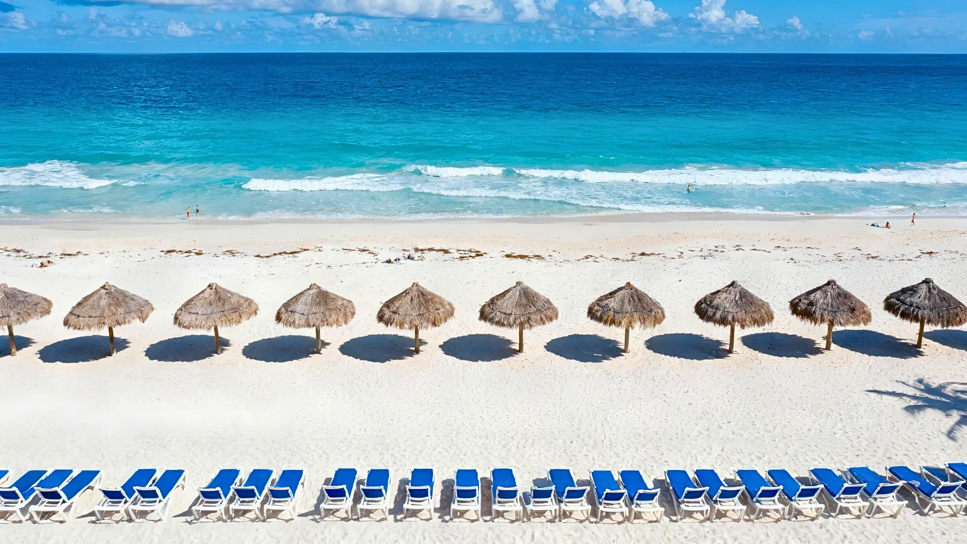 Sandy beach at Golden Parnassus Cancun with turquoise waves, umbrellas, and low seaweed levels.
