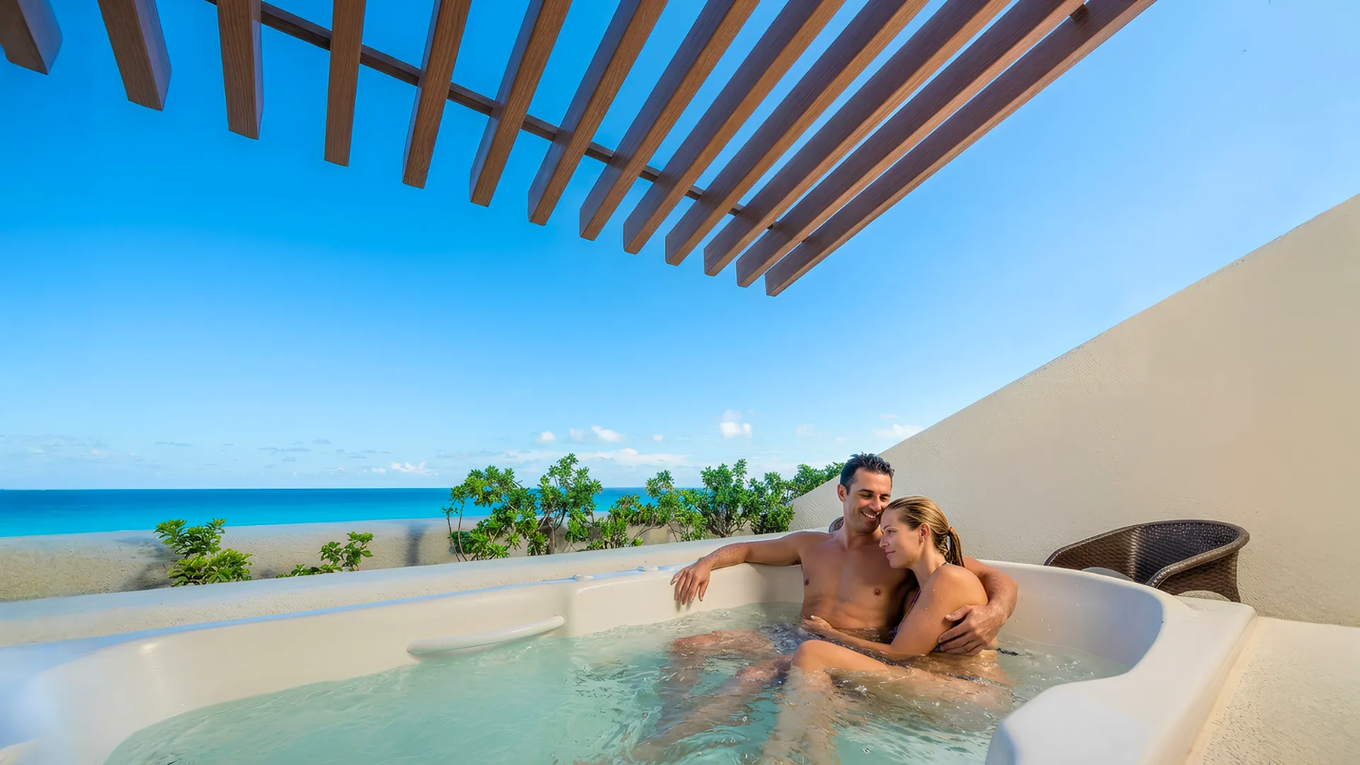 Couple relaxing in a private outdoor hot tub at Royal Solaris Cancun with ocean views and a wooden pergola above.