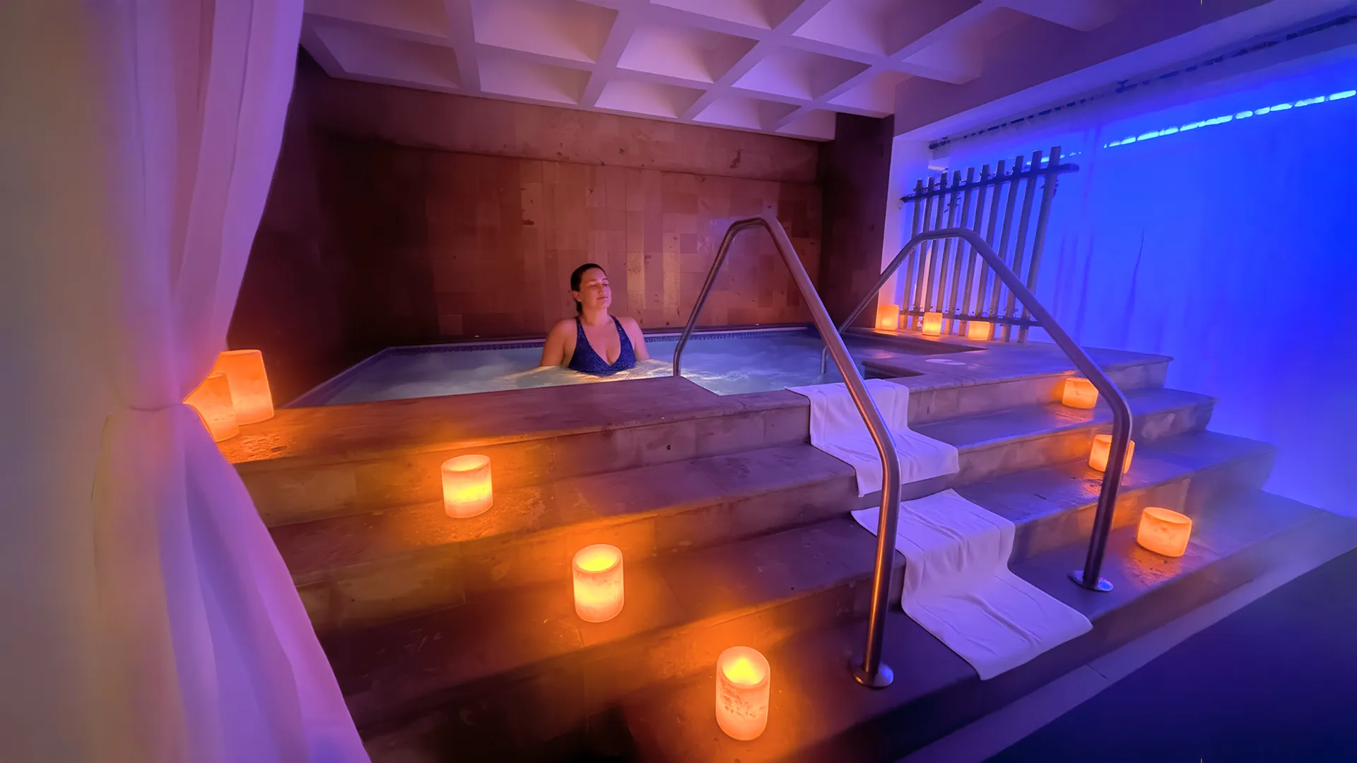 Guest relaxing in a spa hydrotherapy pool surrounded by warm candle lighting at GR Solaris Cancun.