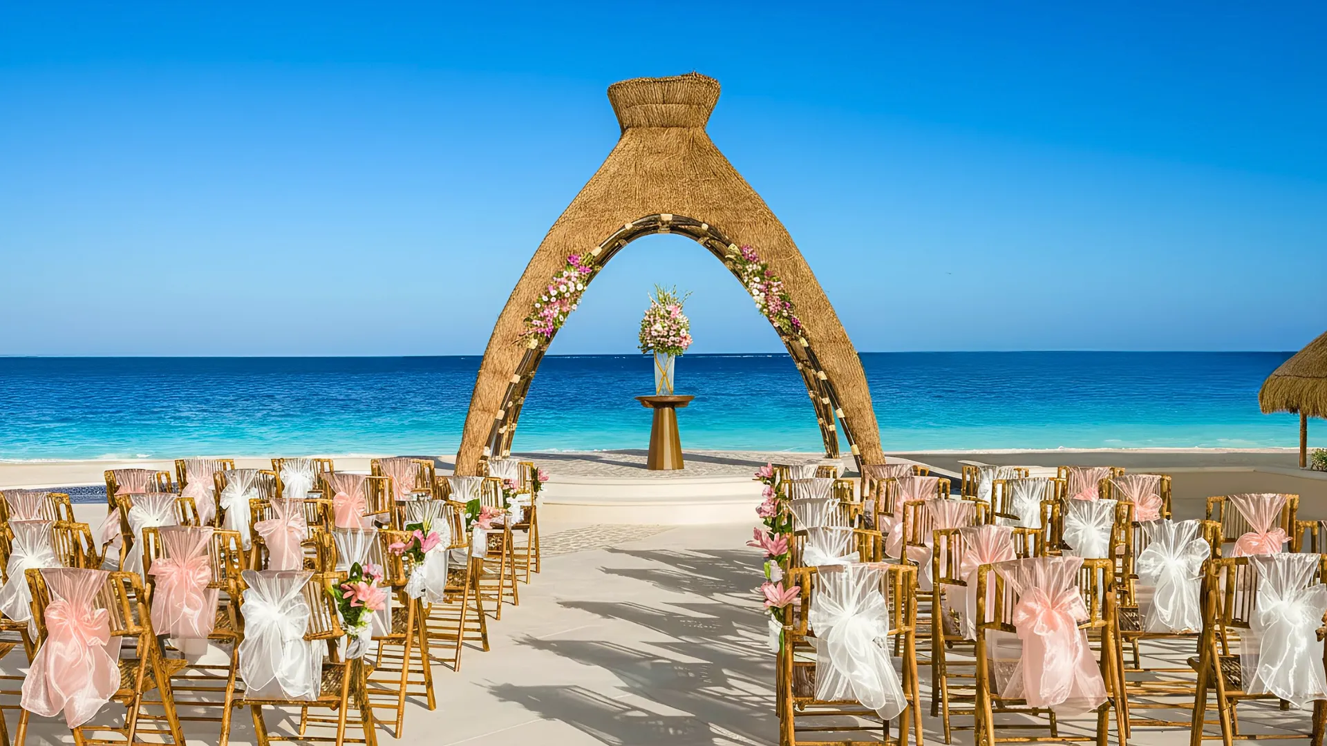 Beach wedding setup at Dreams Riviera Cancun with floral arch and chairs facing the turquoise ocean.