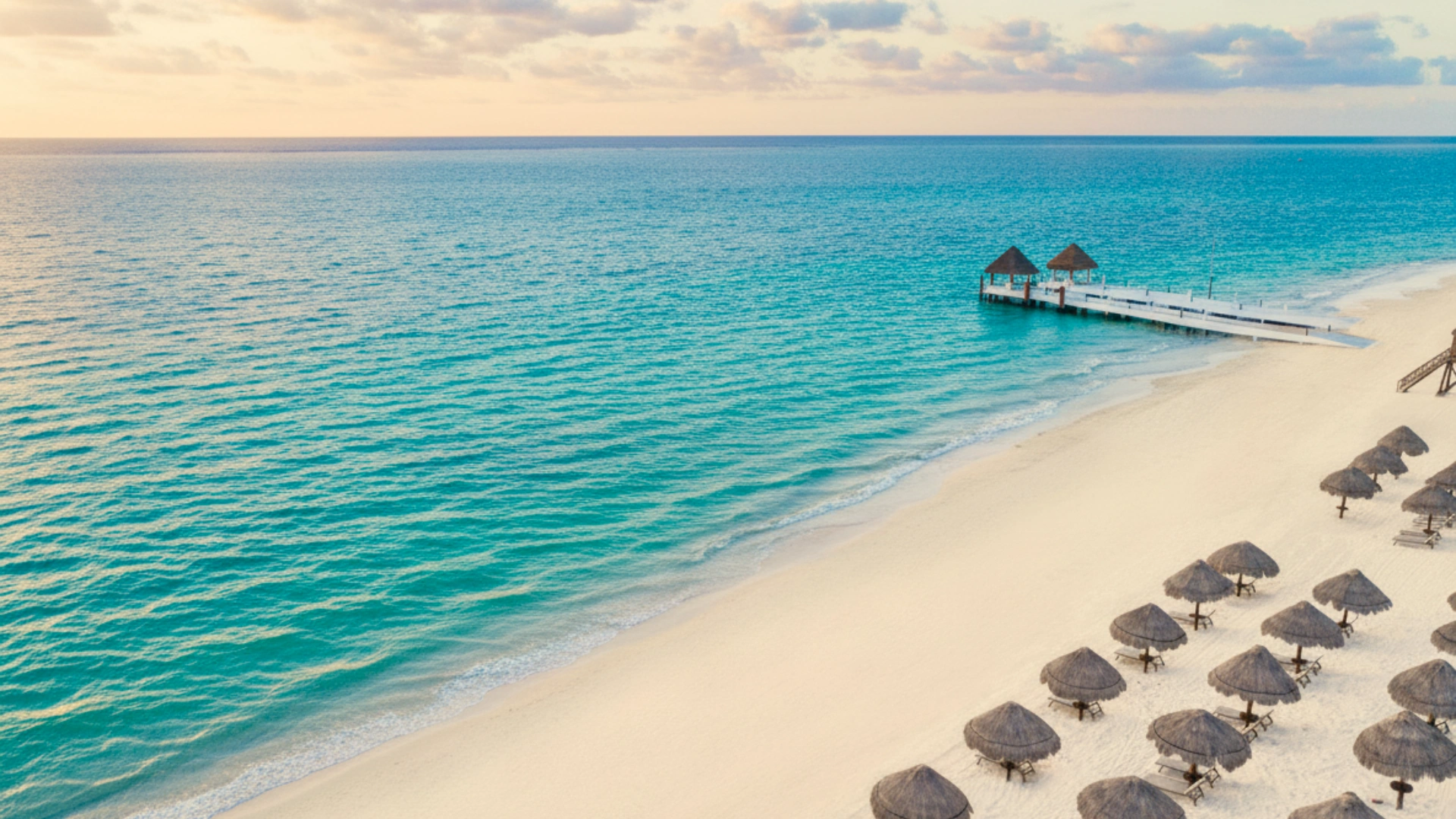 The sandy beach and crystal-clear waters at Excellence Cancun, with sunbeds arranged neatly along the shoreline. 