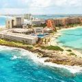 An aerial view of Hyatt Ziva Cancun’s beachfront, showcasing a sandy coastline, turquoise ocean, and multiple resort buildings with palm trees.