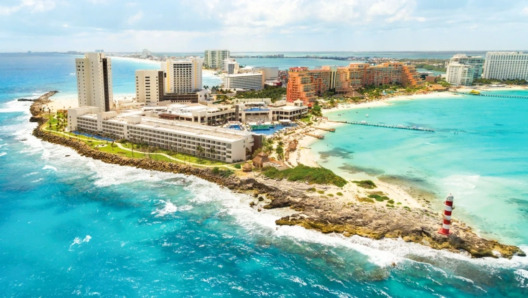 An aerial view of Hyatt Ziva Cancun’s beachfront, showcasing a sandy coastline, turquoise ocean, and multiple resort buildings with palm trees.