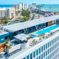 Aerial view of Canopy by Hilton Cancun’s rooftop pool overlooking the turquoise Caribbean Sea and Hotel Zone skyline.