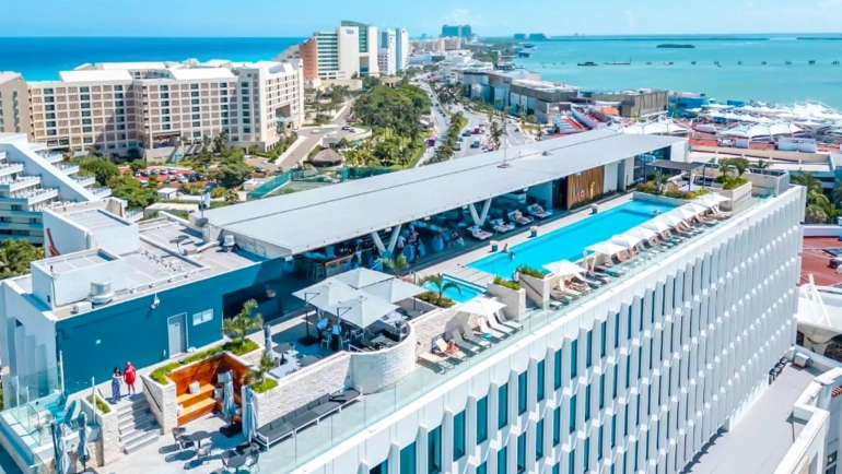 Aerial view of Canopy by Hilton Cancun’s rooftop pool overlooking the turquoise Caribbean Sea and Hotel Zone skyline.