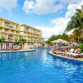 Aerial view of Azul Beach Resort Riviera Cancun showcasing multiple interconnected blue swimming pools with thatched-roof cabanas, white lounge chairs, multi-story resort buildings with balconies, palm trees, and tropical landscaping under a partly cloudy sky.